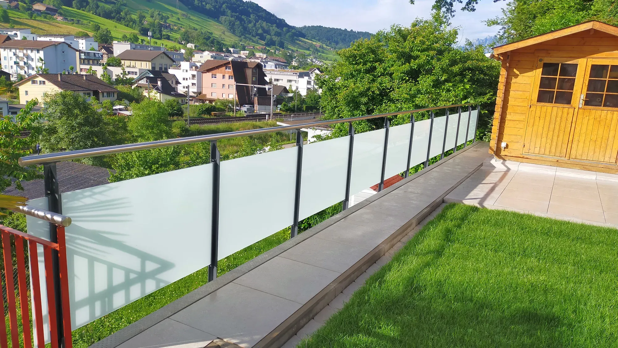 Glasgeländer Classic mit Mattglas entlang eines Gartens, im Hintergrund ein Gartenhaus