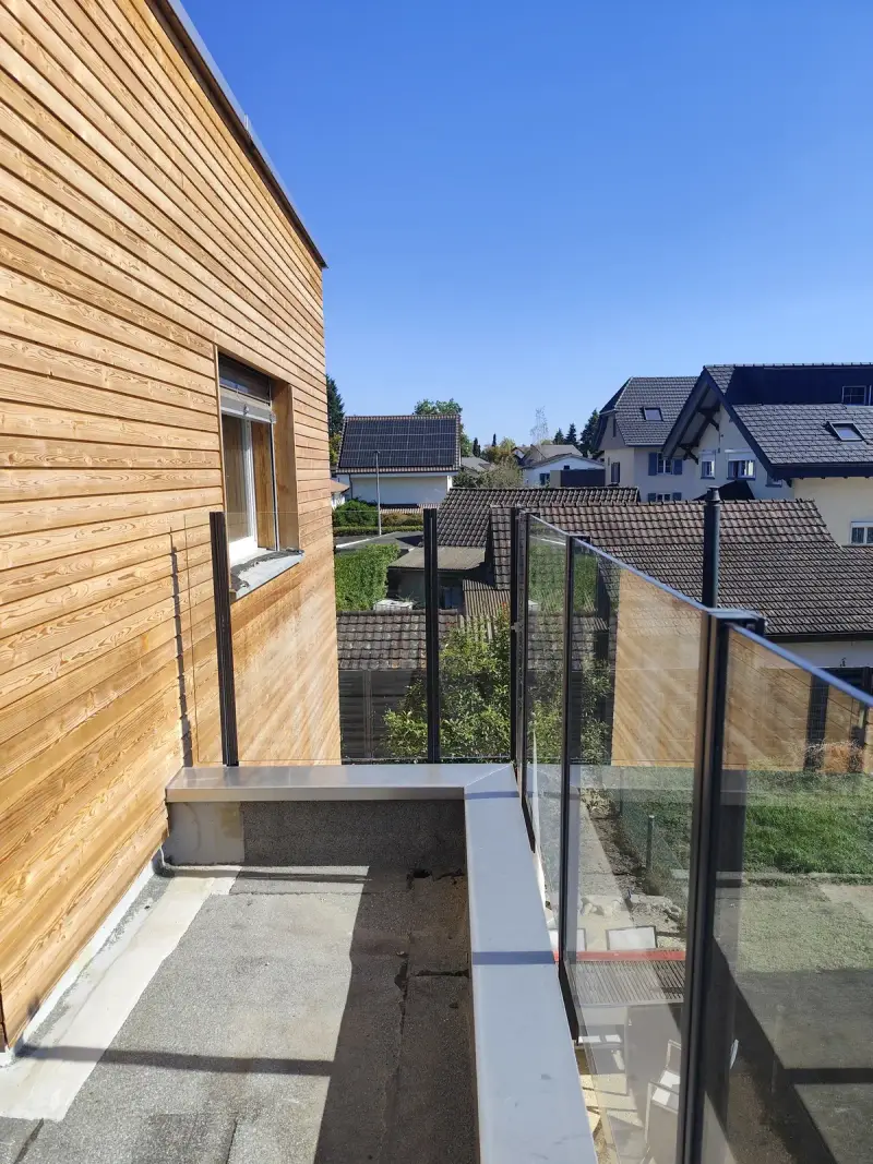 Pfosten des Glasgeländers Pure seitlich an der Dachterrasse befestigt, daneben die Holzfassade